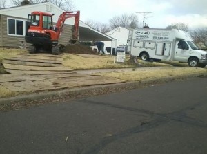 A Professional Tank & Environmental truck and heavy machinery performing a service in front of a home.