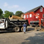 A man walks toward a Professional Tank & Environmental truck parked next to a red excavator in a lot.