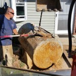 A man in shades holding a shovel helps excavate a dirty and corroded underground tank in front of a home.