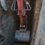 A red excavator digging into a deep dirt hole.