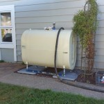 An exterior, cream-colored tank installed snugly between a sidewalk, patio, and home.
