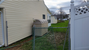 The side of a home with cream colored siding with 2 different types of fencing in view.