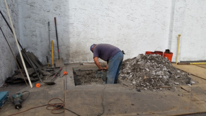 A man in jeans digging into the ground with an assortment of tools in the vicinity.