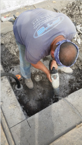 A man standing in a dug-out pit using a tool.